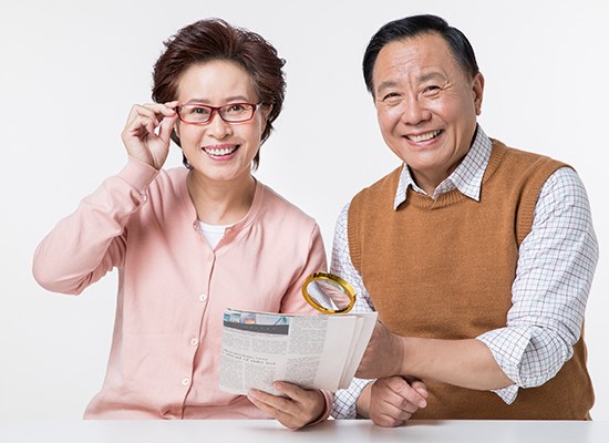 안경을 쓰고 신문과 돋보기를 든 노년 부부